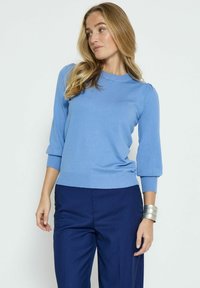 Ljusblå tröja med trekvartsärmar, ribbad halsringning och cuffs, kombinerad med mörkblå randiga byxor. Mjuk textur.