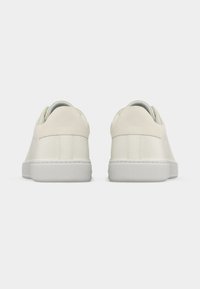 Baskets basses blanches vues de dos avec des panneaux de talon texturés et des semelles plates en caoutchouc sur un fond uni.