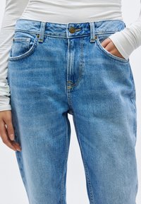 Vaqueros de mezclilla azul claro con un corte relajado, que cuentan con bolsillos delanteros, cierre de botón y un sutil desgaste para dar textura.