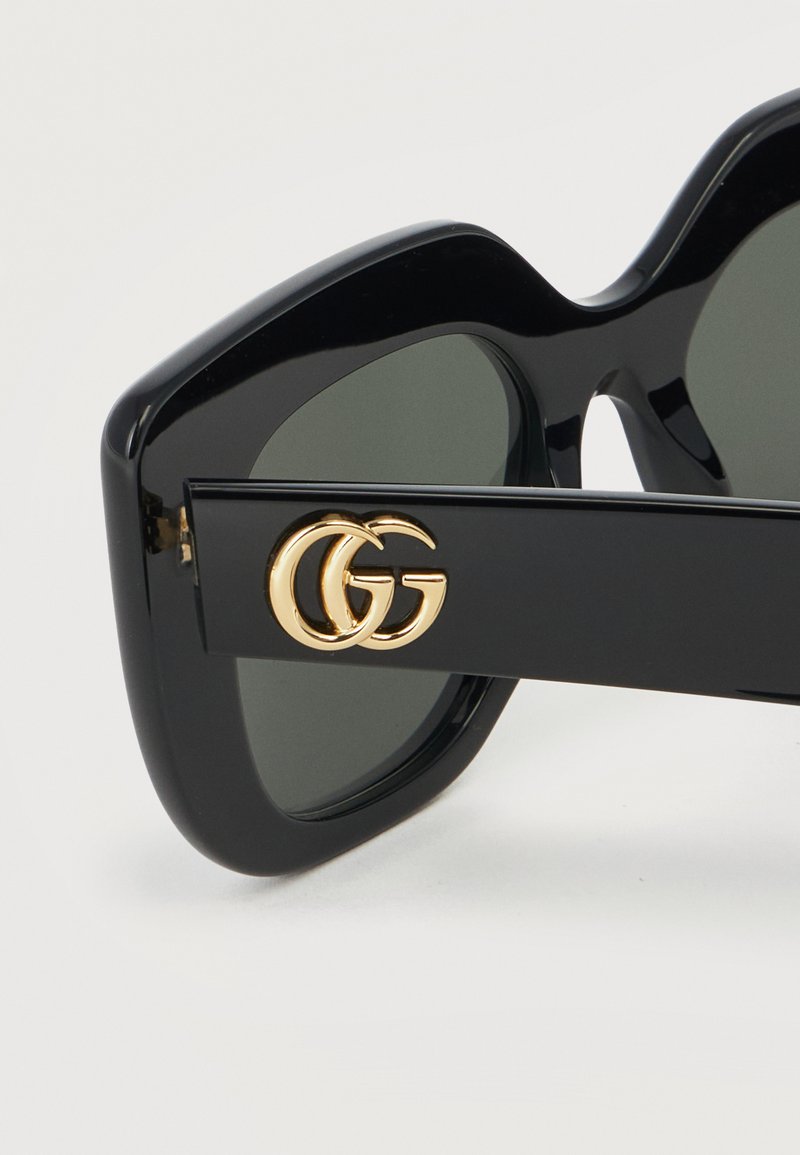 Occhiali da sole oversize neri con lenti scure e logo doppia G dorato sull'asta laterale.