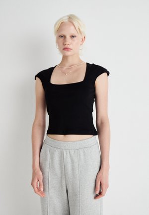Musta lyhythihainen crop-top, jossa on neliönmuotoinen kaula-aukko ja pehmeä kangas. Yhdistetty vaaleanharmaisiin collegehousuihin, joissa on joustava vyötärö.