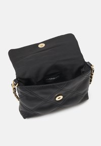 Musta tikattu käsilaukku, jossa on kullanvärinen napsautuslukko ja ketjuhihna. Laukun sisäpuoli on vuorattu mustalla kankaalla. Sisällä näkyy merkkilappu.