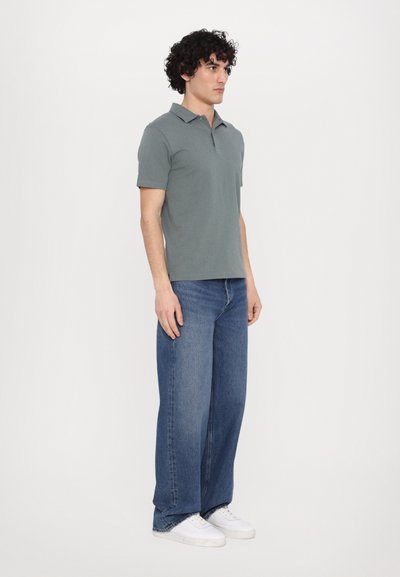 Green cotton polo shirt with short sleeves, paired with loose-fit blue denim jeans and white sneakers. Simple design, minimal accents.