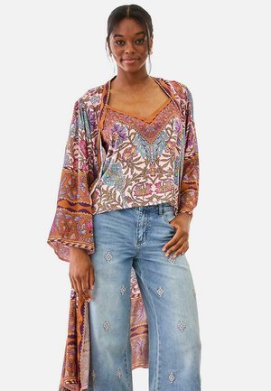 Mujer con chaqueta de estilo kimono estampada con flores y top, combinados con vaqueros de pierna ancha decorados con pequeños parches bordados.