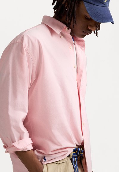 Chemise rose clair à manches retroussées, fabriquée en coton. Présente un col boutonné et un petit logo à l'ourlet.