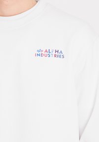 Biała bluza z kolorowym logo "ALPHA INDUSTRIES" na lewej piersi, wykonana z bawełny, z okrągłym dekoltem i ściągaczami przy mankietach.