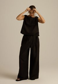 Czarny top bez rękawów w połączeniu z szerokimi spodniami w kolorze czarnym. Gładki, lekki materiał o minimalistycznym designie, bez widocznych wzorów i ozdób.