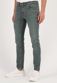 Vihreät denim-farkut, joissa on kapea malli, viisi taskua ja hienovaraiset hihnat. Yhdistetty valkoisiin tennareihin kontrastiksi.