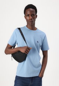 Light blue short-sleeve t-shirt with a small embroidered logo, paired with a black crossbody bag featuring a strap labeled "JACK&JONES."