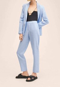 Blazer tailored di colore azzurro chiaro e pantaloni abbinati realizzati in tessuto testurizzato, indossati sopra un body nero e abbinati a sandali neri.