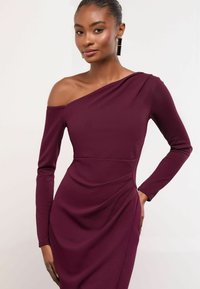 Haljina bez naramenica u burgundiji s dugim rukavima, koja ističe prilagođenu siluetu i drapirani teksturirani donji dio, naglašavajući čiste linije.