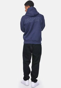 Navy blue hoodie with a large "DROPSIZE" print on the back, paired with black pants and white sneakers. Soft fabric and casual fit.