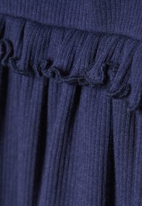 Marineblauwe lichte stof met verticale ribbels, voorzien van een gekruide rand langs de bovenkant. Zachte textuur met een gemiddelde val, geschikt voor casual kleding.
