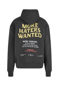 Black hoodie with yellow, white, and red text on back reading "MORE HATERS WANTED" and a provocative hiring message beneath.