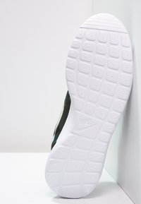 Černá a zelená sportovní obuv s texturovanou bílou gumovou podrážkou s mřížkovým vzorem a logem Nike. Jednoduchý design a nízký profil.