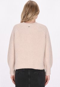 Lichtbeige gebreide trui met een textuurpatroon, raglanmouwen en een ronde halslijn, die eindigt op de taille, gecombineerd met donkere spijkerbroek.