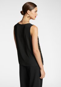 Top senza maniche nero con dettagli in pizzo dorato intrecciato lungo i lati, texture liscia e vestibilità comoda, visto da dietro.