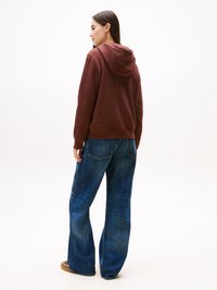 Moleton castanho-avermelhado com capuz, de corte descontraído, combinado com calças de ganga azuis de perna larga. Textura suave, design simples e estilo casual.