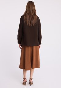 Brązowa wełniana kurtka o prostym kroju, zestawiona z beżową spódnicą i obcasami w zwierzęcy wzór. Posiada rozcięcie z tyłu oraz boczne kieszenie.
