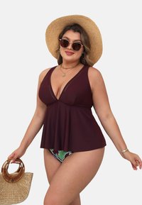 Bordeaux tankini-top met een v-hals, decoratieve stiksels en een uitlopend zoom; gecombineerd met bloemige bikini-broekjes en een strohoed.