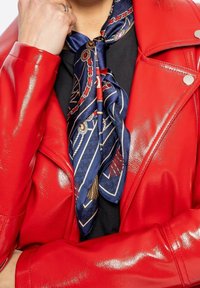 Personne portant une veste en cuir rouge brillante et un haut noir, accessoirisée d'une écharpe en soie bleu marine à motif nouée autour du cou.