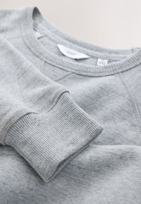 Jasnoszara bluza z długim rękawem z prążkowanymi mankietami i dekoltem, pokazująca metki wewnątrz kołnierza.