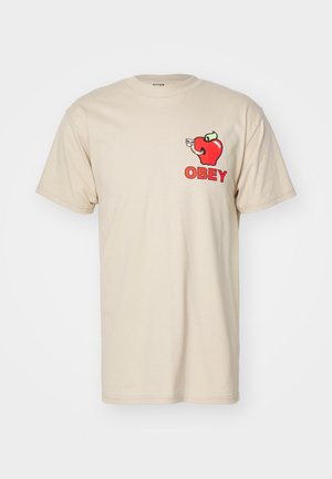 Beige cotton t-shirt featuring a red apple graphic with an elephant and the word "OBEY" in bold letters. Relaxed fit, short sleeves.