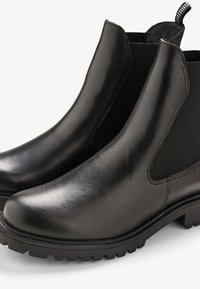 Botas Chelsea de cuero negro con paneles laterales elásticos, puntera redondeada y suela de goma texturizada con un patrón de tracción en zigzag.