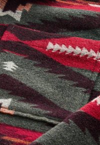 Gros plan d'un tissu en laine avec des motifs géométriques en tons rouge, gris, blanc et violet foncé.