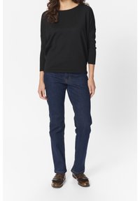 Haut noir côtelé à manches longues, associé à un jean en denim bleu et des chaussures marron avec des détails à franges. Design simple et coupe droite des jambes.