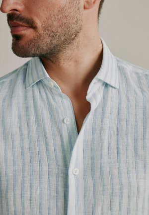 Prim-plan al feței inferioare și gâtului unui bărbat care poartă o cămașă cu nasturi cu dungi albastre deschise și albe, cu nasturele de sus desfăcut.