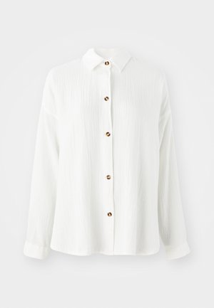 Fehér, hosszú ujjú ing texturált anyagból, gombos elejével, gallérral és barna gombdíszítéssel. Puha, hétköznapi dizájn.