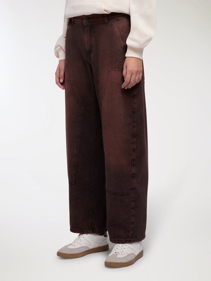 Pantaloni in denim marrone a gamba larga con finitura testurizzata, caratterizzati da grandi tasche frontali e vita alta, abbinati a scarpe da ginnastica bianche.