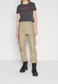 Mörkgrå t-shirt med röd text, beige cargobyxor med flera fickor och svarta snörkängor med en kraftig sula.