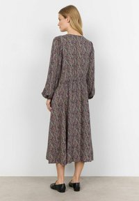 Langarmige jurk met bloemenpatroon in donkere kleuren, accentueerde taille, vloeiende rok en ronde halslijn. Draag met zwarte platte schoenen.