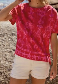 Haut rouge à manches courtes orné d'un motif homard et feuilles aux nuances de rose, avec une bordure d'étoiles de mer à l'ourlet, assorti à un short blanc.