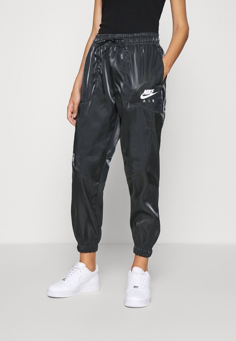 Joggers légers, noirs et brillants, avec une taille élastique et des poignets élastiques, ornés d'un logo 'Nike Air' blanc sur la cuisse gauche.