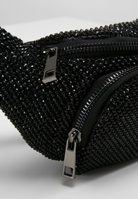 Pochette en tissu noir perlé avec deux curseurs de fermeture éclair argentés et des fermetures éclair noires sur un fond clair uni.