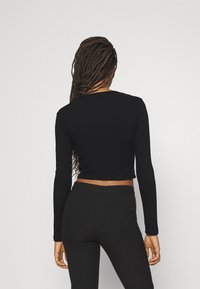 Schwarzes, kurz geschnittenes Langarmoberteil aus glattem Stoff, mit Rundhalsausschnitt und taillierter Silhouette, kombiniert mit passenden schwarzen Leggings.
