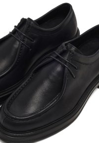 Scarpe in pelle nera con una texture liscia, punta tonda e minimal lace. Presentano una suola a contrasto e accenti di cucitura discreti.