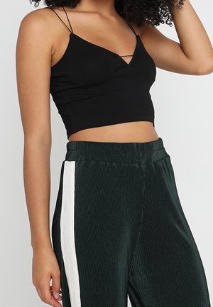 Czarny krótki top z cienkimi ramiączkami i dekoltem w kształcie litery V, zestawiony z ciemnozielonymi prążkowanymi spodniami z białym paskiem po boku.