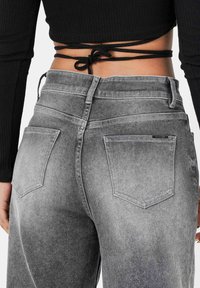 Vaqueros de mezclilla gris de talle alto con un lavado desgastado, bolsillos traseros y textura suave. Top negro anudado visible en la cintura.