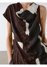 Haut sans manches noir et blanc à motif abstrait avec une texture froissée porté par une personne avec un bras visible.