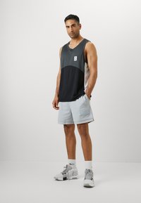 Sport tank top features a color-block design in gray and black. Paired with light gray shorts and gray athletic shoes with white accents.