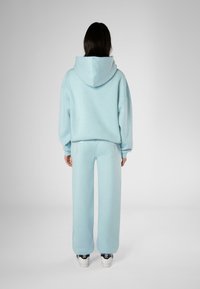 Sudadera azul clara con capucha; combinada con pantalones de chándal de pierna ancha a juego que presentan detalles de acento. Tejido suave con una textura lisa.