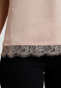 Haut rose clair en tissu lisse avec une délicate bordure en dentelle à l'ourlet, ornée de motifs floraux et de bords festonnés, associé à un tissu noir.