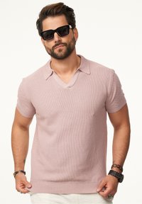 Kurzarmpoloshirt mit V-Ausschnitt in Hellrosa, mit einem strukturierten Stoff und geripptem Saum, kombiniert mit schwarzen Sonnenbrillen.