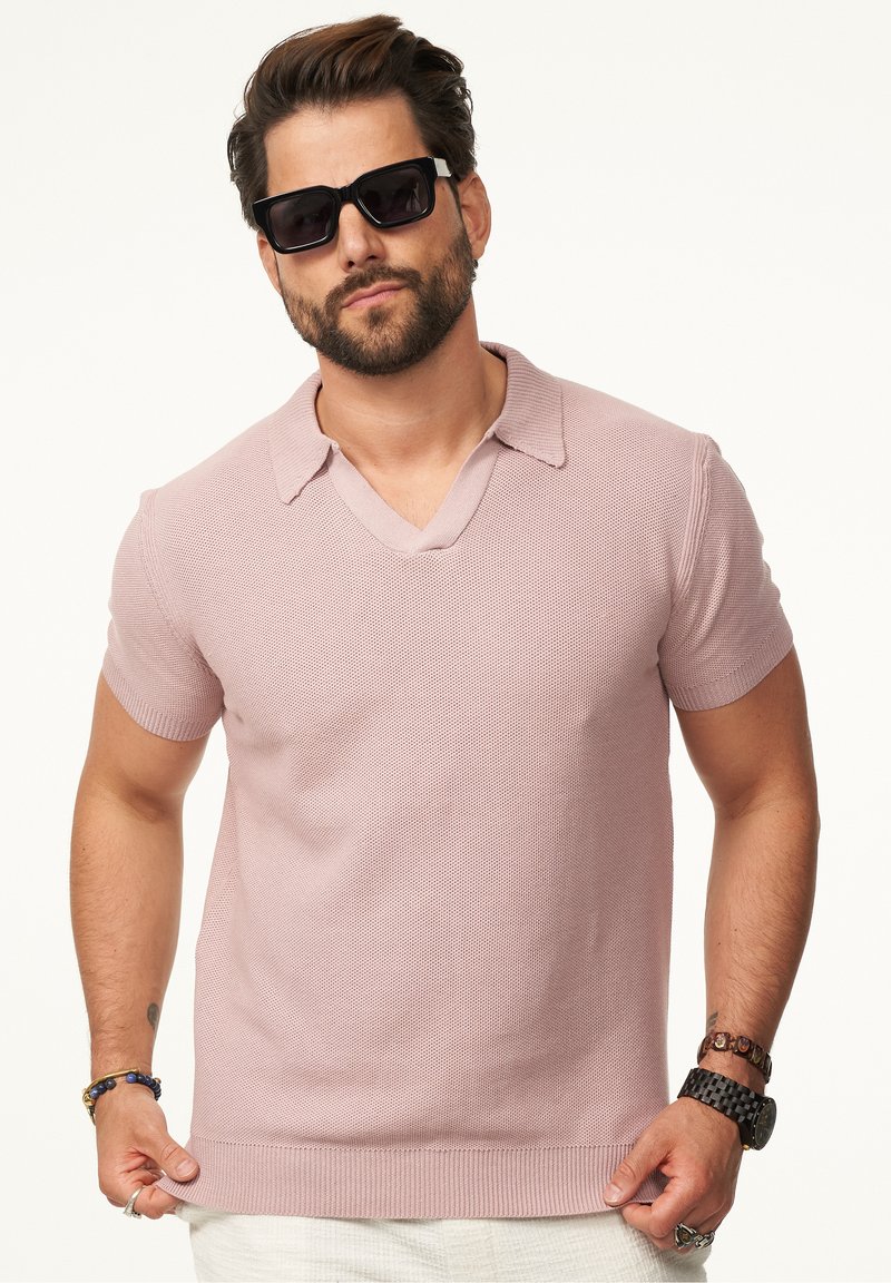 Kurzarmpoloshirt mit V-Ausschnitt in Hellrosa, mit einem strukturierten Stoff und geripptem Saum, kombiniert mit schwarzen Sonnenbrillen.