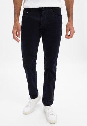 Navy Corduroy-Hosen mit schlanker Passform, aus strukturiertem Stoff, mit fünf Taschen, Metallknöpfen und kombiniert mit weißen Turnschuhen.