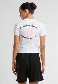 Camiseta de algodón blanca con un gráfico de resplandor solar rosa y texto en la parte trasera. Pantalones cortos negros con detalles rosados en los lados.